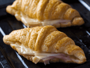Two croissants with ham and cheese on a baking sheet.