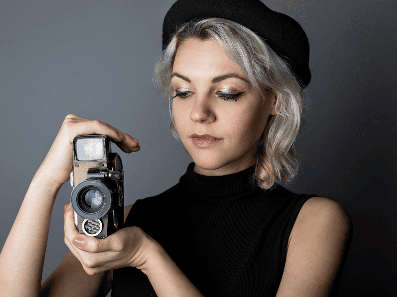 A woman holding a camera on a gray background.