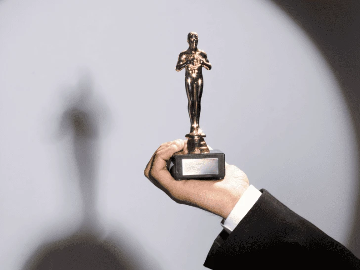 A hand holding an oscar statuette in front of a shadow.
