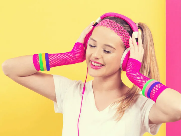 A young woman wearing headphones listening to music on a yellow background.