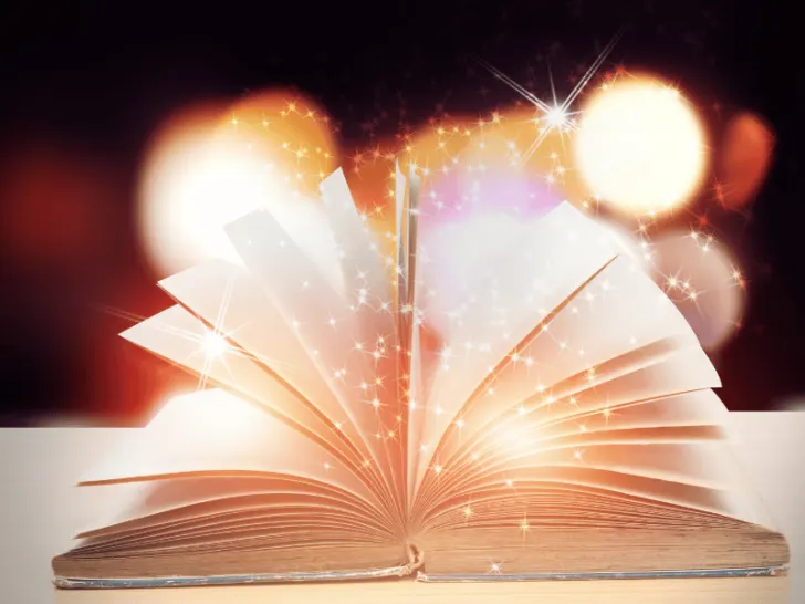 An open book on a table with light coming out of it.