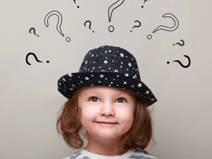 A little girl wearing a hat with question marks above her head, sparking curiosity.