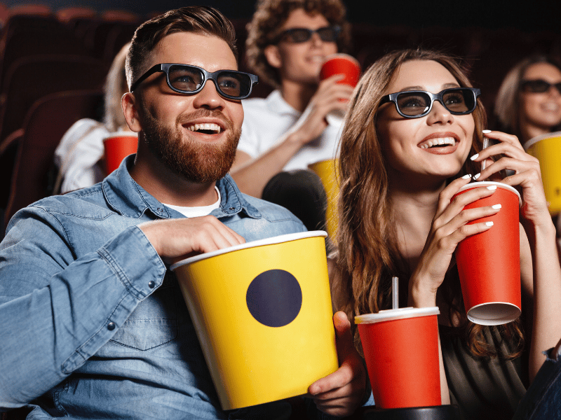 A group of people sitting in a movie theater wearing 3D glasses, discussing their favorite superhero films and explaining the reasons behind their choices.