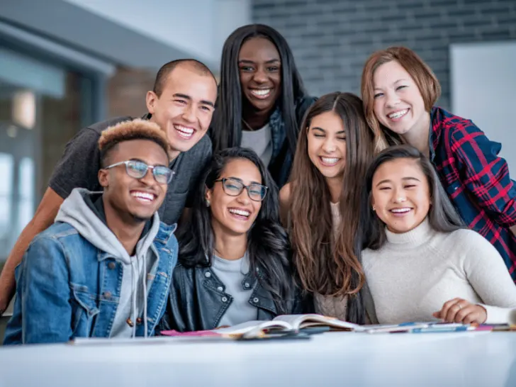 A diverse group of young people smiling at each other in a classroom, highlighting the importance of diversity in the world.