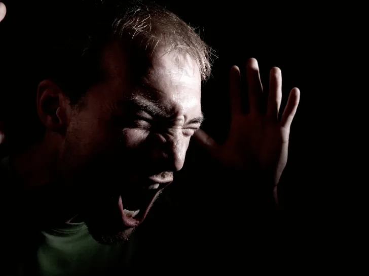 A man shouting loudly in an obscure setting.