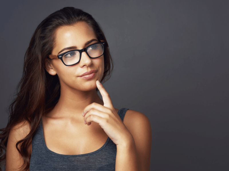 Young woman in glasses posing with her finger on her chin, contemplating favorite things.