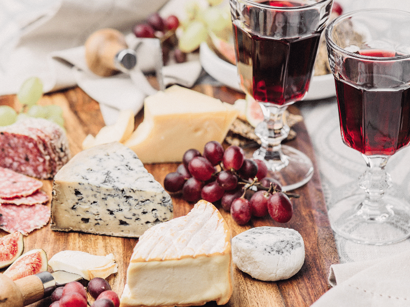 A cutting board with cheese and wine glasses.