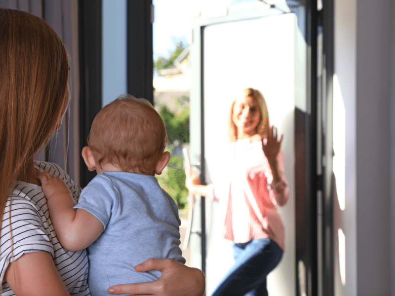 An au pair holding a baby in front of an open door.