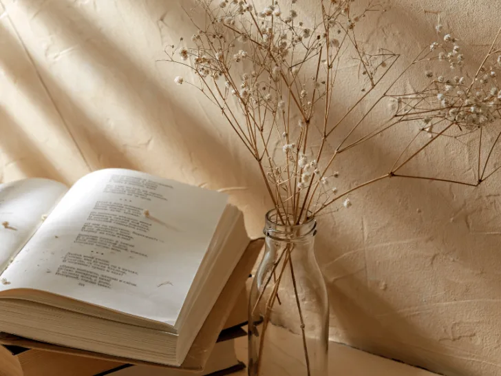 An open book on a table with a vase of dried flowers for poetic inspiration.