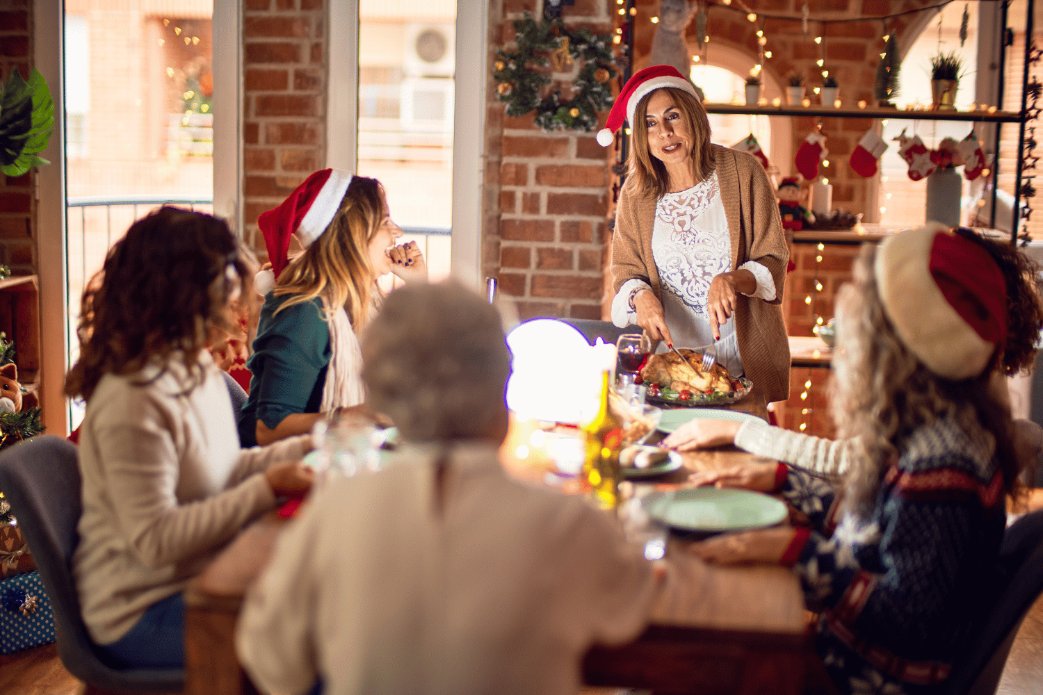 A group of women in santa hats sitting around a table, discussing their favorite tradition.