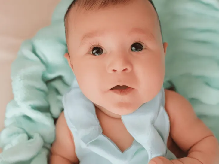 A baby is laying on a blue blanket looking at the camera, showcasing one of the popular choices for a favorite name trend.