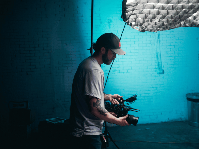 A man holding a camera in front of a blue light, crafting a compelling narrative for his documentary filmmaking project.